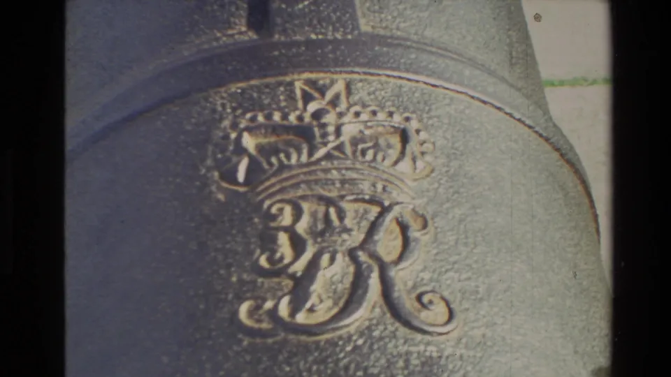 The frame lingers on the cannon’s cast crown and intertwined monogram, with visible 8mm grain and soft focus.
