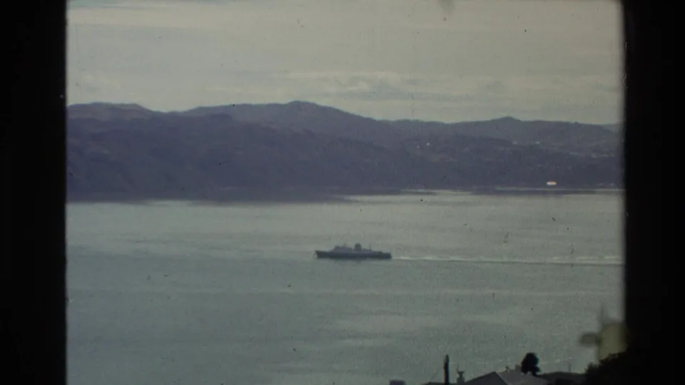 1981 New Zealand 8mm frame with a ferry or passenger vessel moving across a calm bay beneath distant hills.