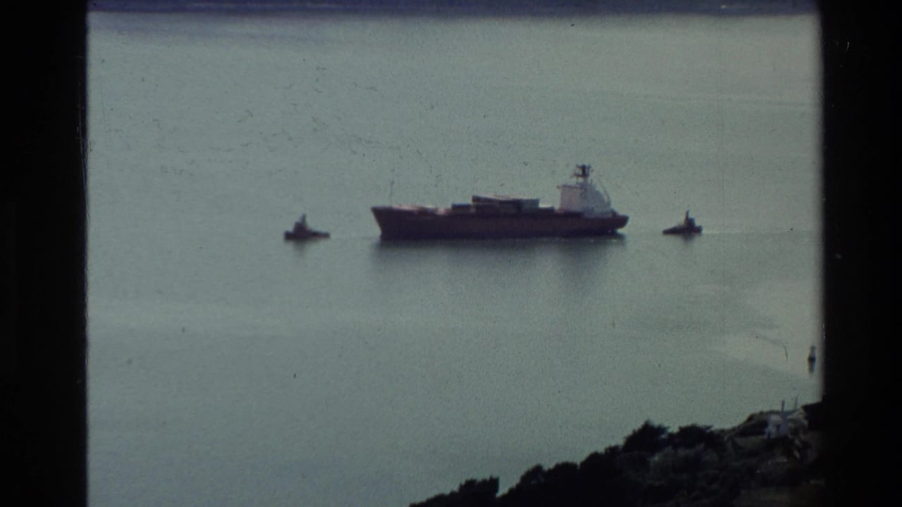 Distant harbor vessel on a calm New Zealand bay, flanked by smaller boats and seen through 8mm frame edges.
