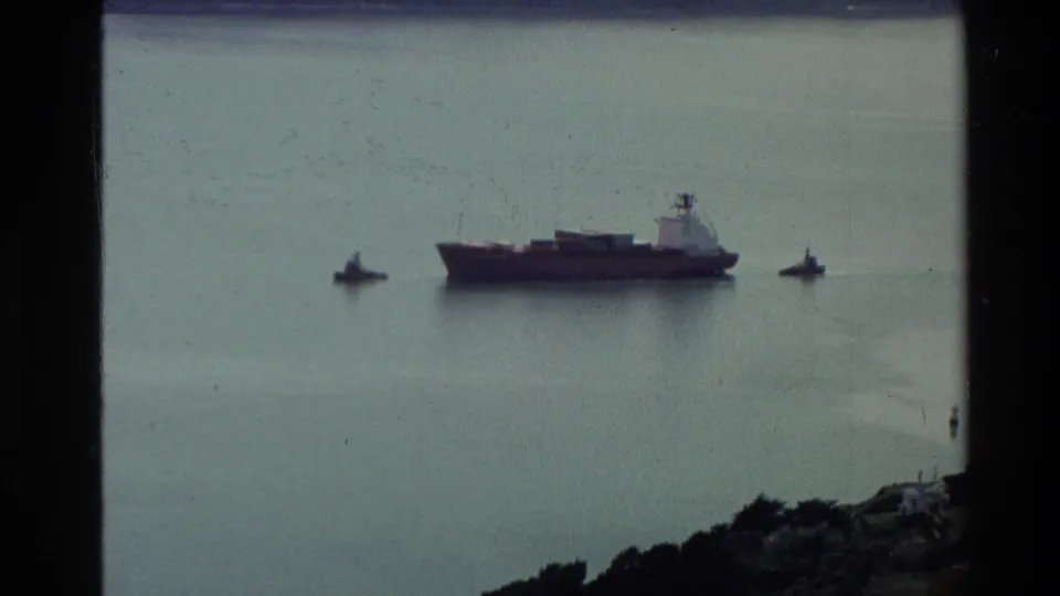 Distant harbor vessel on a calm New Zealand bay, flanked by smaller boats and seen through 8mm frame edges.