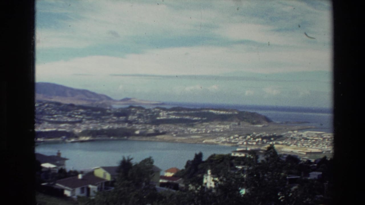 Harbor and shoreline settlement viewed from above with sea and hills beyond.