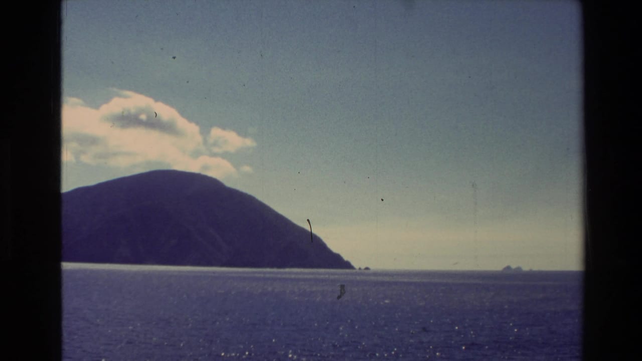 1982 New Zealand 8mm frame showing a dark coastal island across open water under a bright sky, viewed from a boat.
