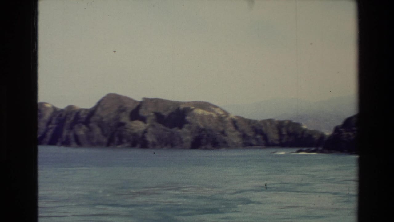 Rocky shoreline and calm blue-green water seen through a vertical film frame divide.