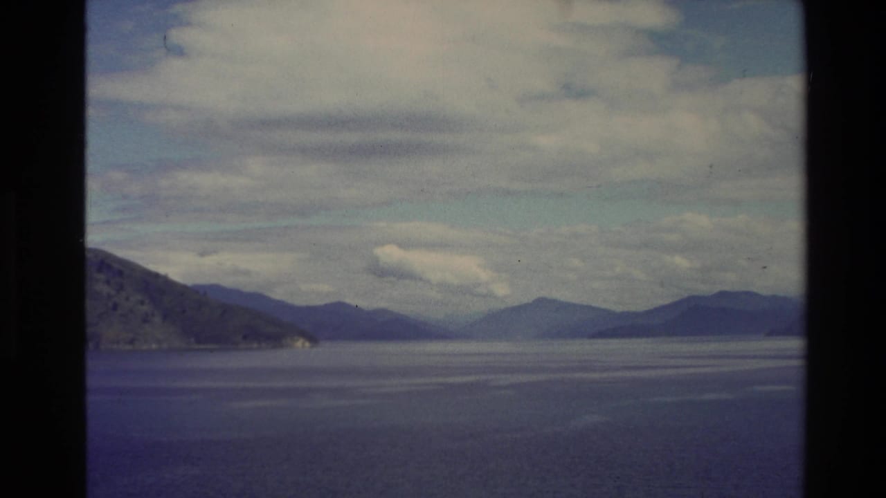 1982 New Zealand 8mm view of calm coastal water with distant hills and soft clouds across the horizon.