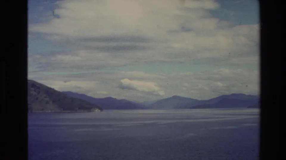 1982 New Zealand 8mm view of calm coastal water with distant hills and soft clouds across the horizon.