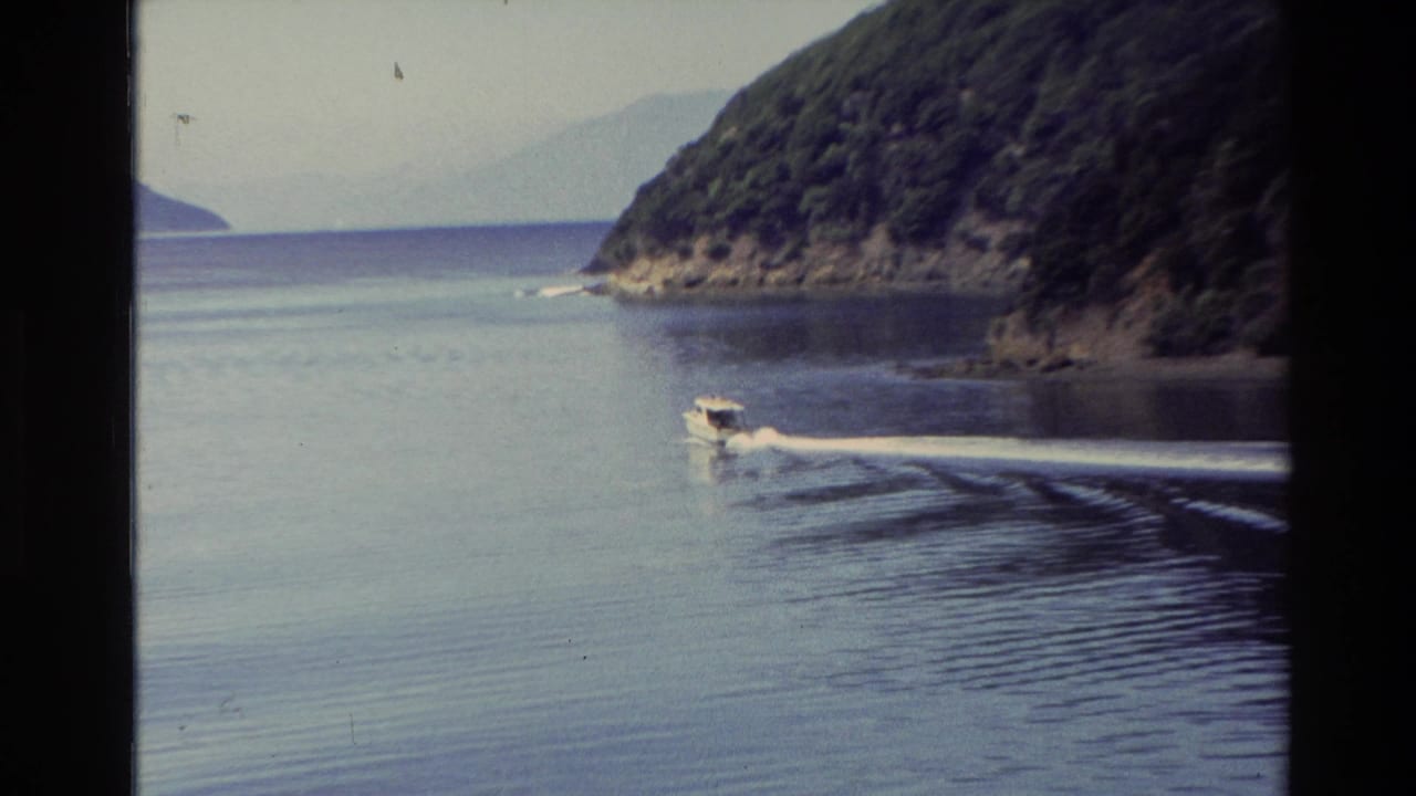 1982 New Zealand 8mm frame showing a small motorboat skimming across calm lake water below wooded hills.