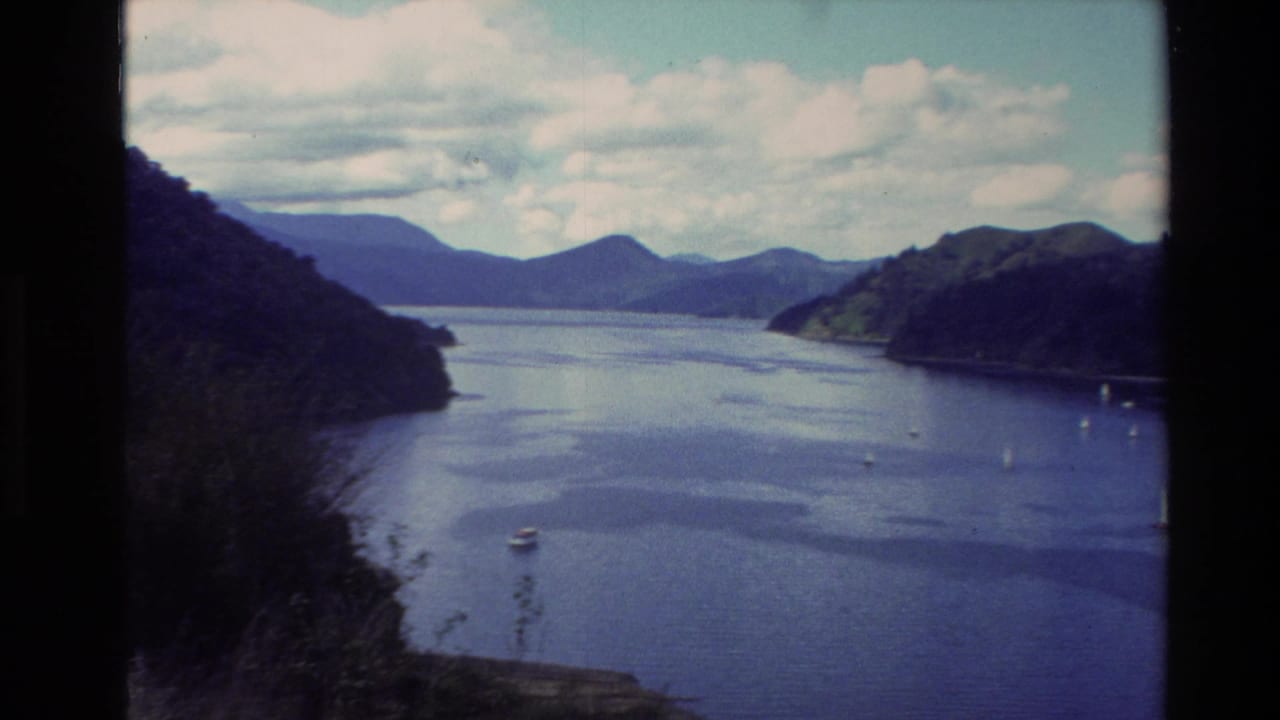 Wide lake view with forested hills, distant mountains, and small boats on the water.