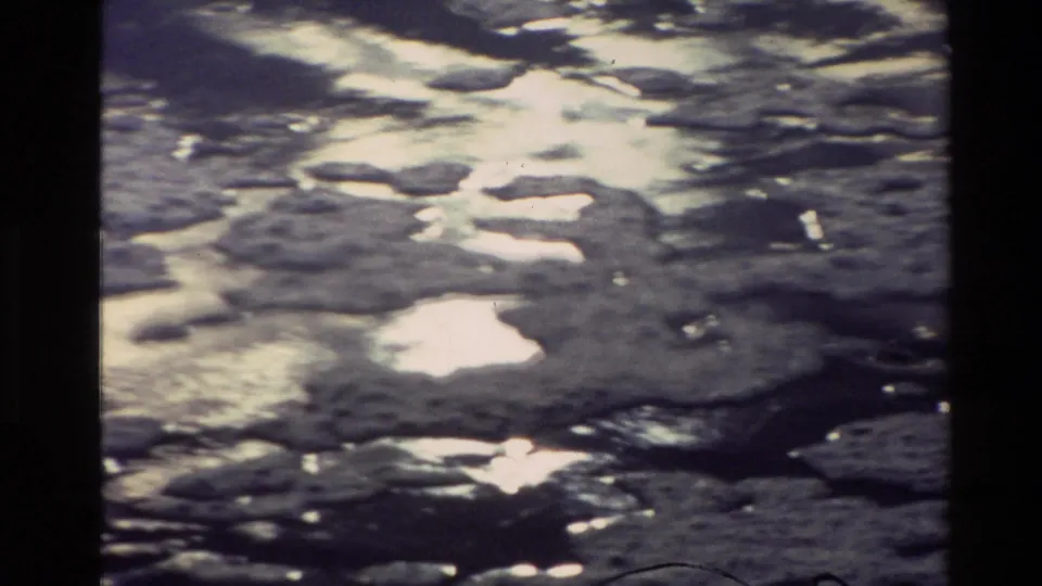 1982 New Zealand 8mm frame showing rippled river water with strong reflected light and dark floating patches.