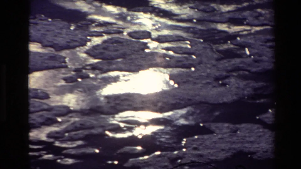 8mm home-movie frame of a New Zealand river surface with clustered dark patches and shimmering reflected light.
