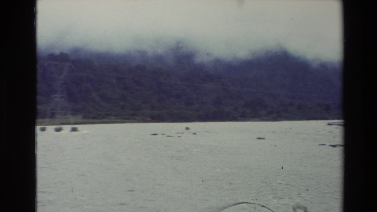 1982 New Zealand 8mm frame showing a wide riverbed beneath misty forested mountains and an overcast sky.