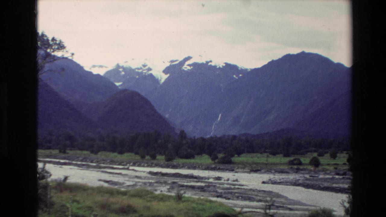 1982 New Zealand home-movie view of a braided river below dark forest and snow-capped mountains.