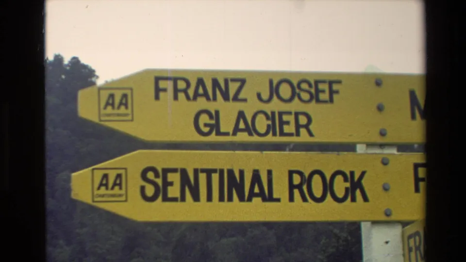 Close view of yellow New Zealand directional signs for Franz Josef Glacier and Sentinel Rock, with AA logos visible.