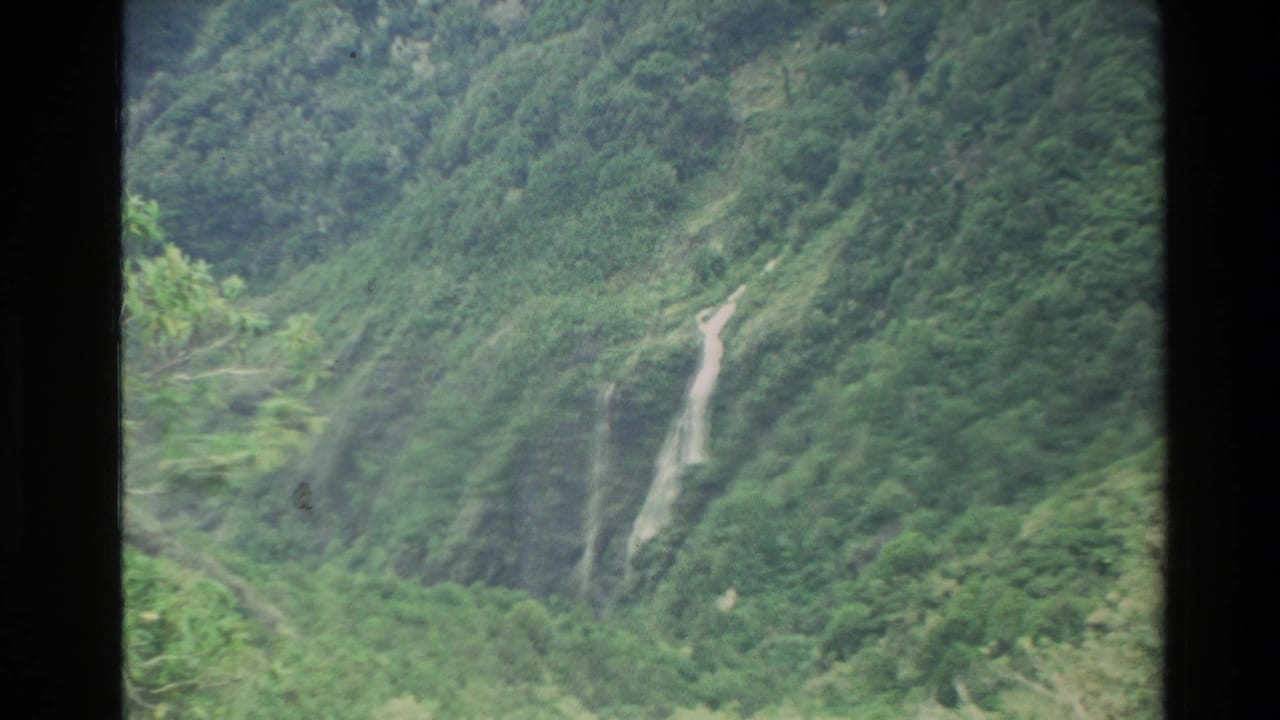 Green mountain slope with a narrow waterfall running down a steep valley wall.