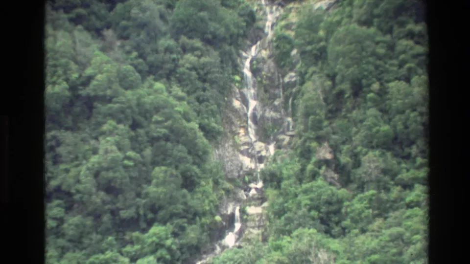 1982 New Zealand 8mm frame showing a closer multi-step waterfall dropping through lush forested terrain.