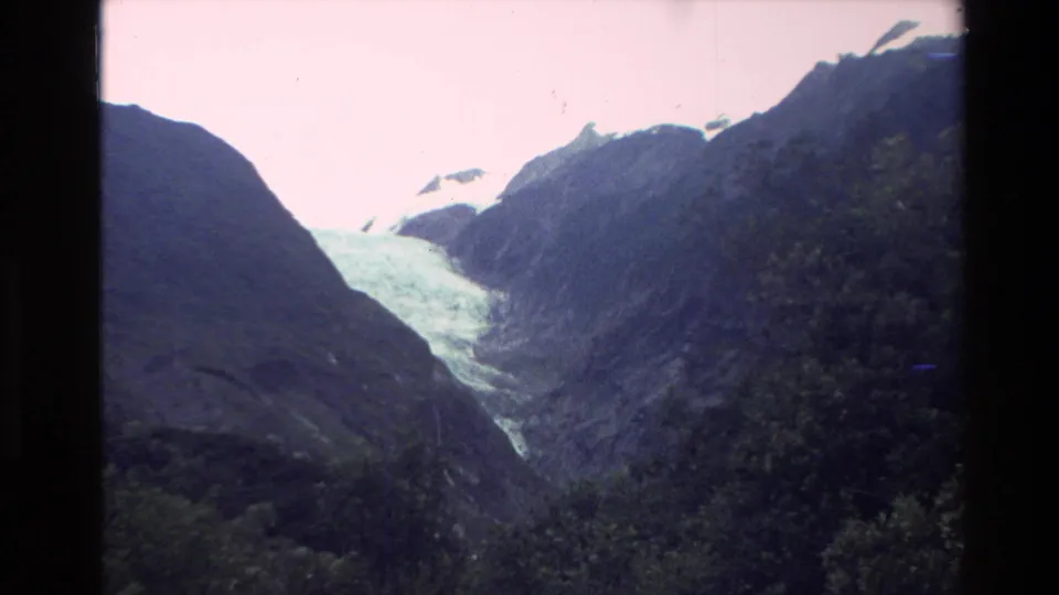 1982 New Zealand 8mm view of dark mountain slopes framing a pale glacier or snowfield in the distance.