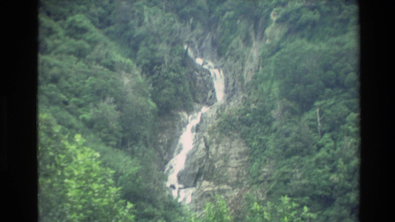 1982 New Zealand 8mm frame showing white water dropping down a forested mountain cliff.