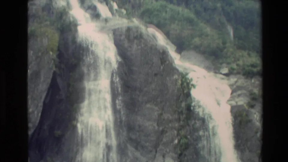 New Zealand 8mm frame from 1982 with white water running down a dark rock face and greenery at the edge.