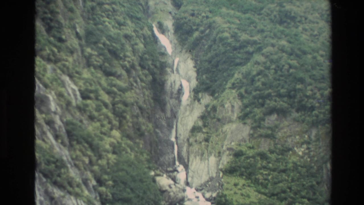 Waterfall dropping through a green rocky mountain gully.