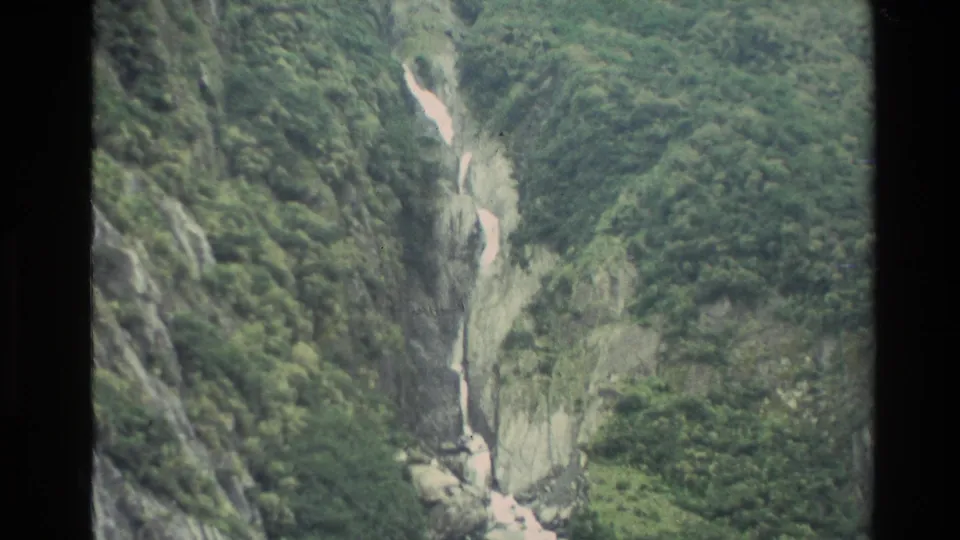 1982 New Zealand 8mm frame showing a white waterfall descending through a steep, forested rocky gully.