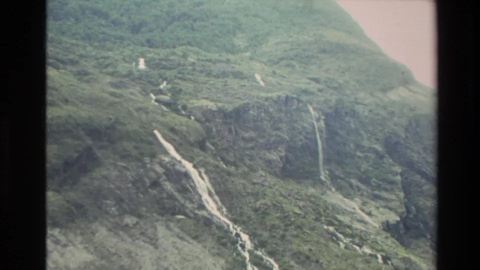 1982 New Zealand 8mm frame showing a wider view of waterfalls crossing a forested mountain slope.