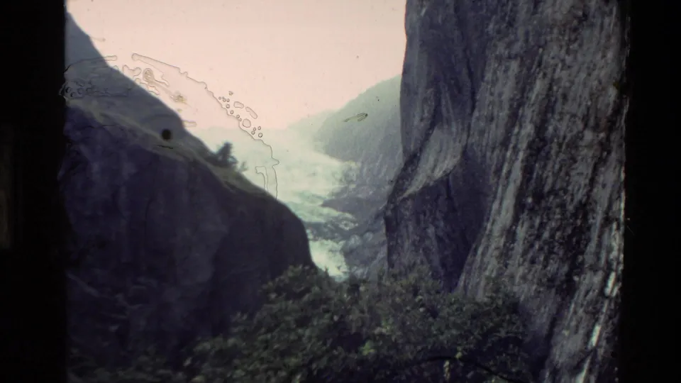 1982 New Zealand 8mm frame showing a narrow mountain valley between sheer cliffs, with shrubs and pale sky visible.