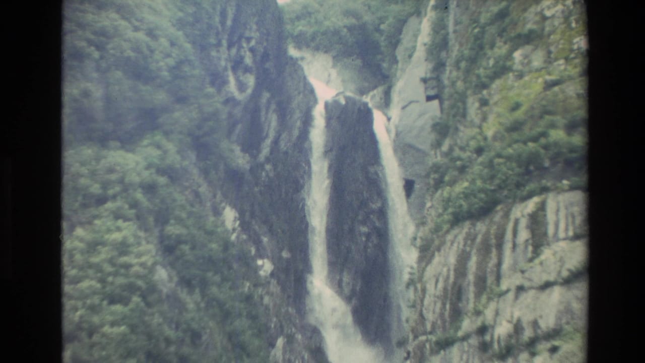 1982 New Zealand 8mm frame showing white water falling through a narrow rocky gorge bordered by green vegetation and grey cliffs.