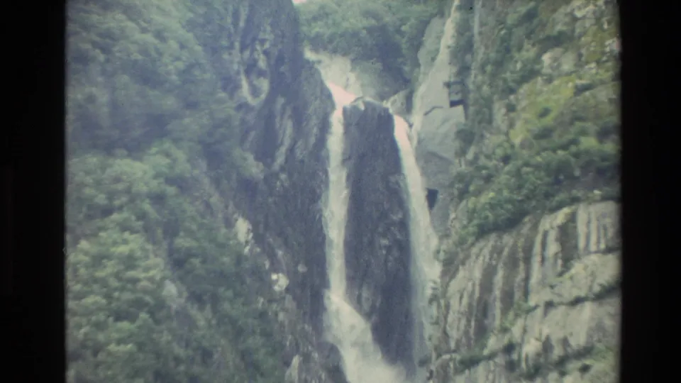 1982 New Zealand 8mm frame showing white water falling through a narrow rocky gorge bordered by green vegetation and grey cliffs.