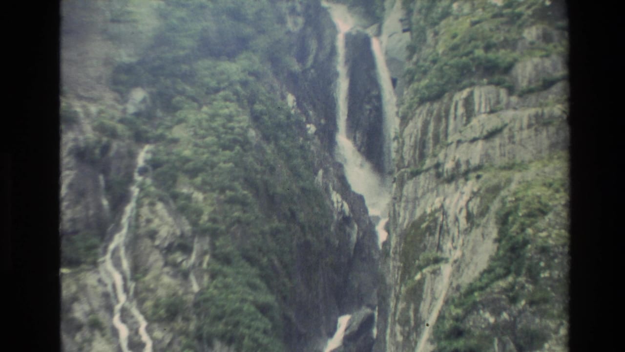 Tall waterfall and side cascades running down a rocky mountain gorge.