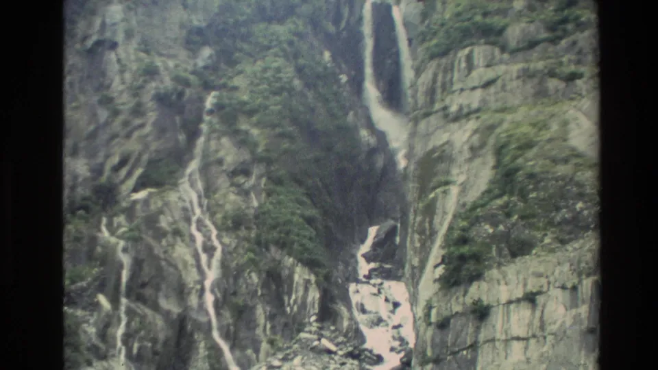 1982 New Zealand 8mm frame showing white cascades running down grey rock toward a stony riverbed at the base of the gorge.
