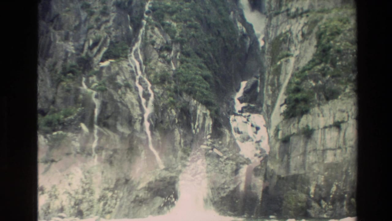 1982 New Zealand 8mm frame showing steep rocky cliffs with pale waterfalls and green moss across the stone.