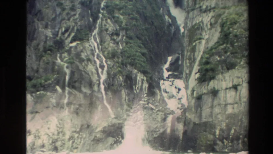 1982 New Zealand 8mm frame showing steep rocky cliffs with pale waterfalls and green moss across the stone.