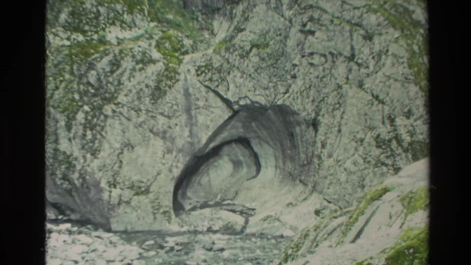 1982 New Zealand 8mm frame showing a pale rock face with a dark hollow cavity and small stones at the base.