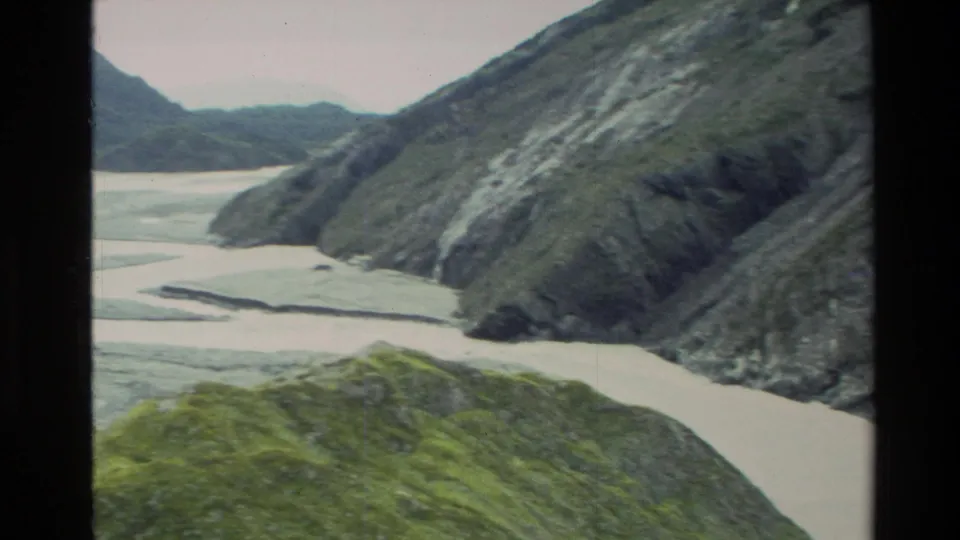 1982 New Zealand 8mm view across braided muddy river channels in a rugged mountain valley.
