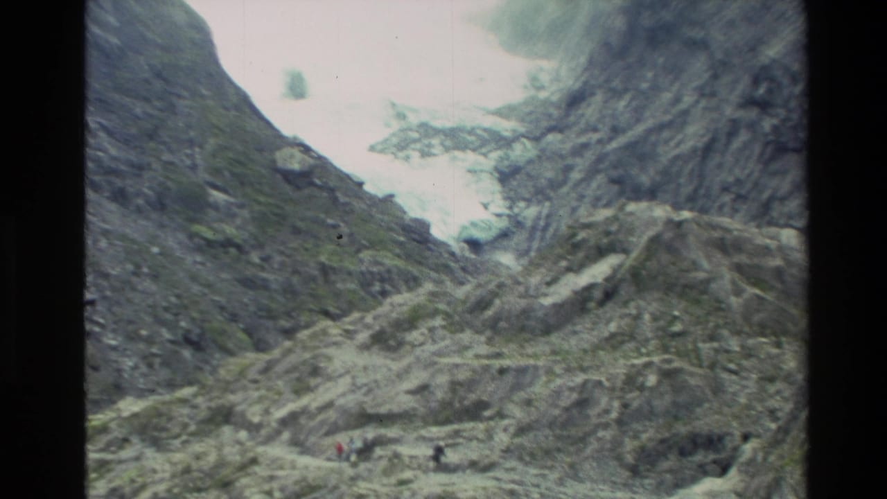 Rocky alpine valley with glacier ice and small hikers near the lower slope.