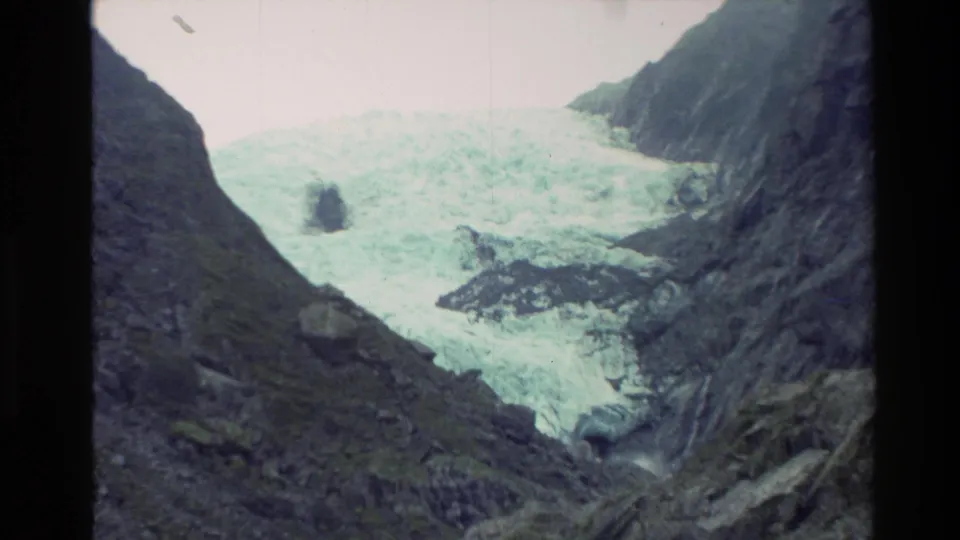1982 New Zealand 8mm view of a broad glacier face set between shadowed rock slopes under bright overcast light.