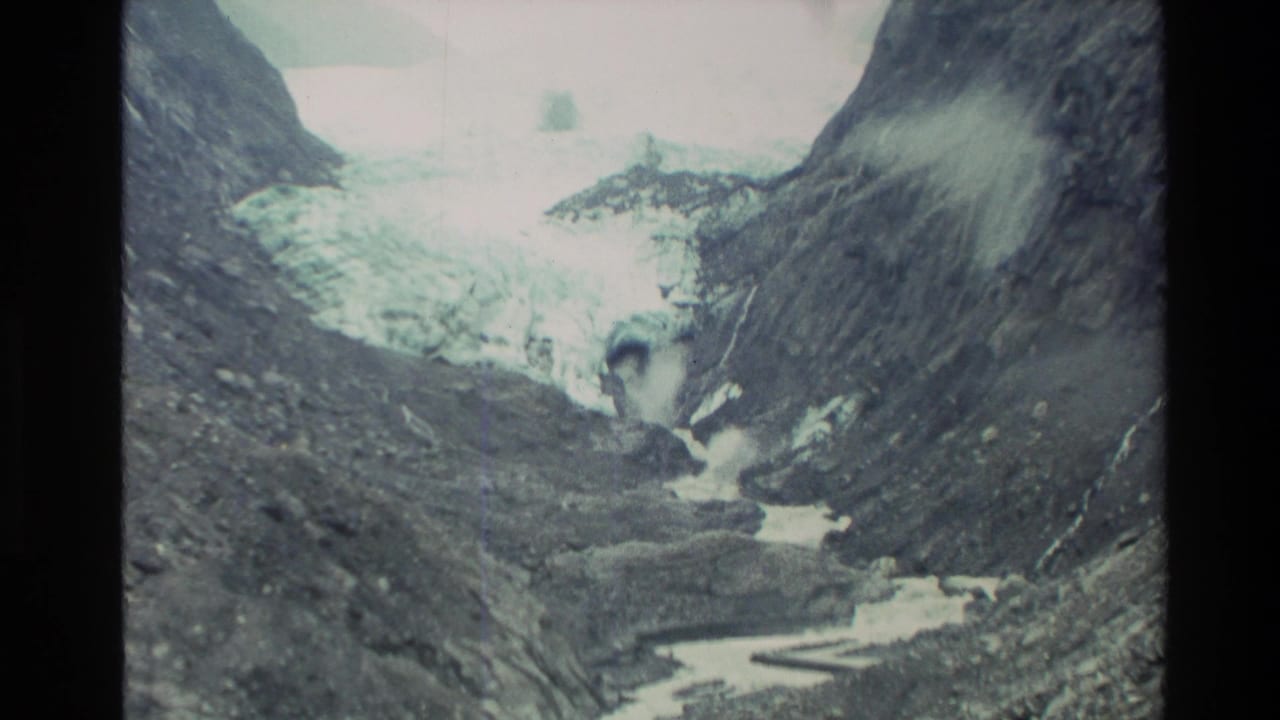 Rocky alpine valley with glacier ice and a pale stream below.