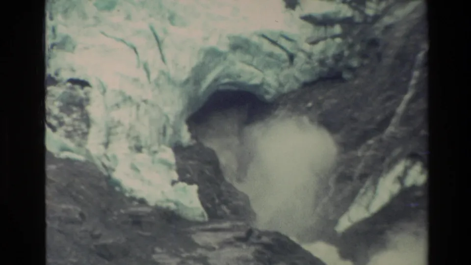 1982 New Zealand 8mm frame with turbulent meltwater surging from a cave-like ice opening in a rocky mountain channel.