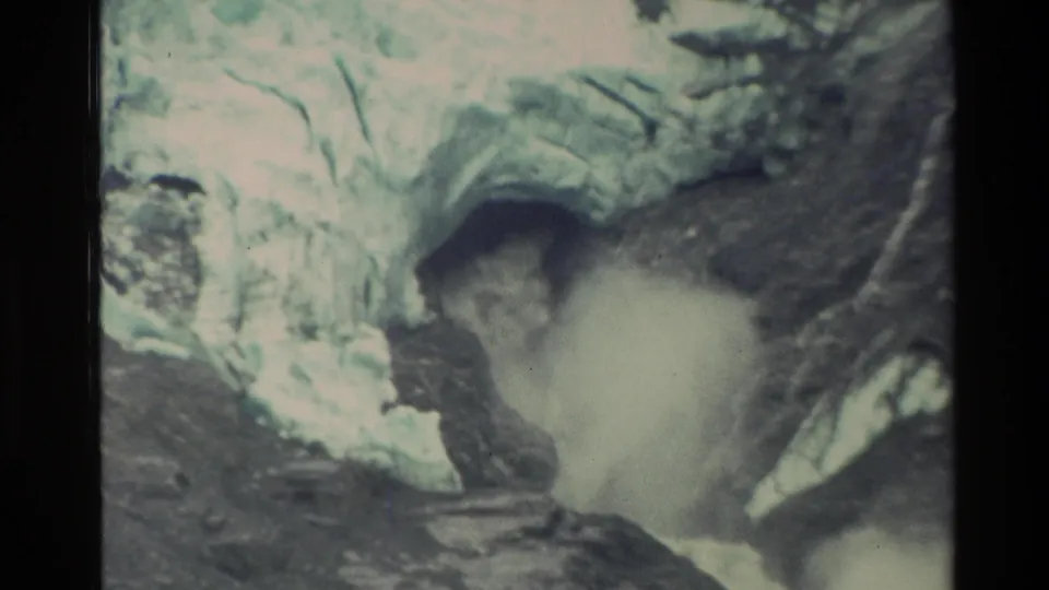 1982 New Zealand 8mm frame showing pale ice above a dark opening where meltwater blasts into a steep rocky chute.