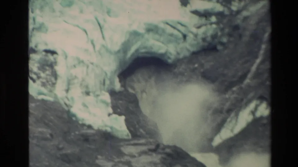 1982 New Zealand 8mm frame with a wide foamy surge below a shadowed ice opening, bordered by pale ice and dark rock.