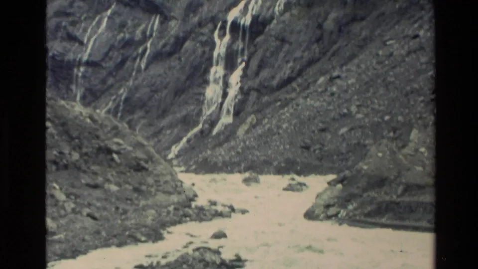 1982 New Zealand 8mm frame with a narrow waterfall dropping down a rocky mountain slope into a pale rushing stream.