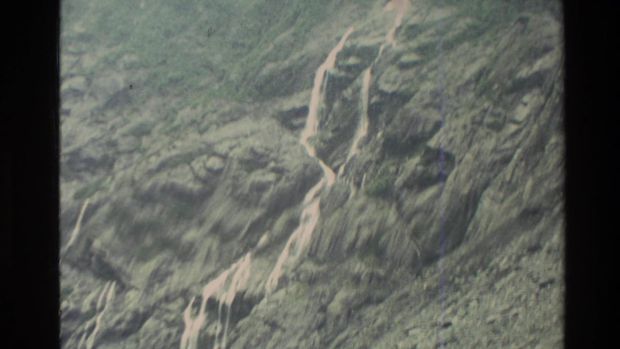 1982 New Zealand 8mm frame showing eroded mountain terrain with bright runoff lines across dark rock and vegetation.