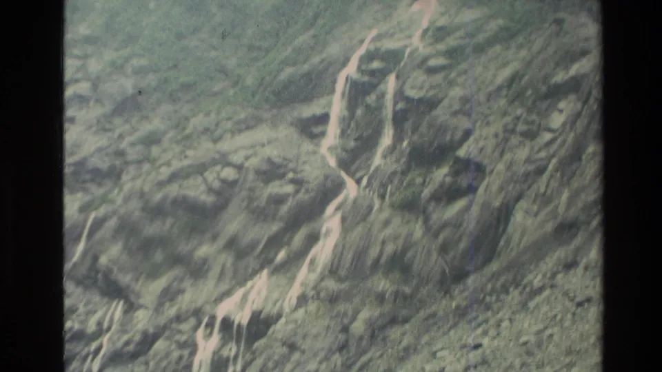 1982 New Zealand 8mm frame showing eroded mountain terrain with bright runoff lines across dark rock and vegetation.