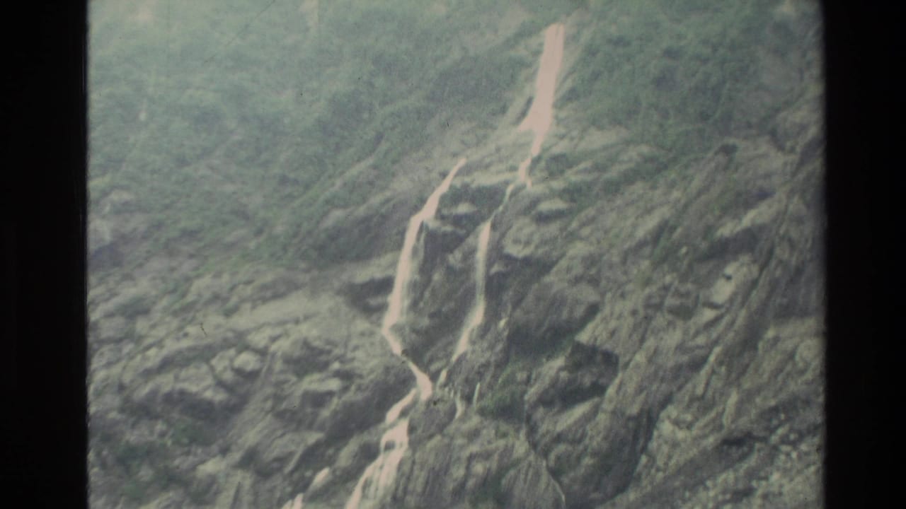 Rocky mountain face with narrow white runoff streams descending through gullies.