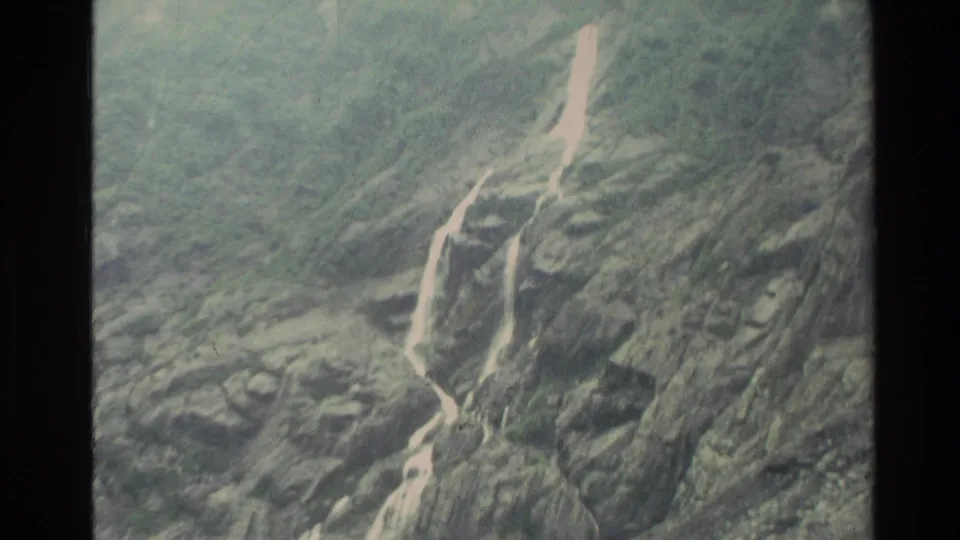 1982 New Zealand 8mm view of white runoff lines descending across a rugged green-gray mountain slope.