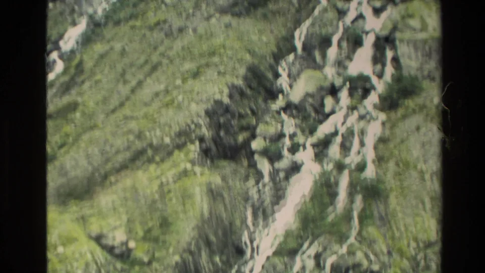 1982 New Zealand 8mm frame with motion blur as bright runoff channels descend a rocky, vegetated mountainside.