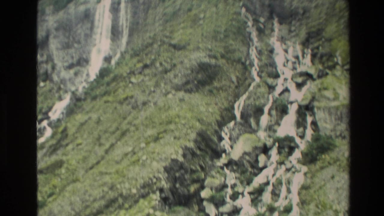 1982 New Zealand 8mm frame showing waterfalls dropping across a green, rocky cliff face.