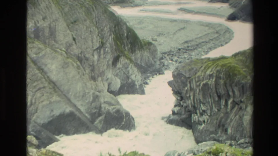 1982 New Zealand home-movie frame showing a rocky gorge and winding river channel below cliffs.