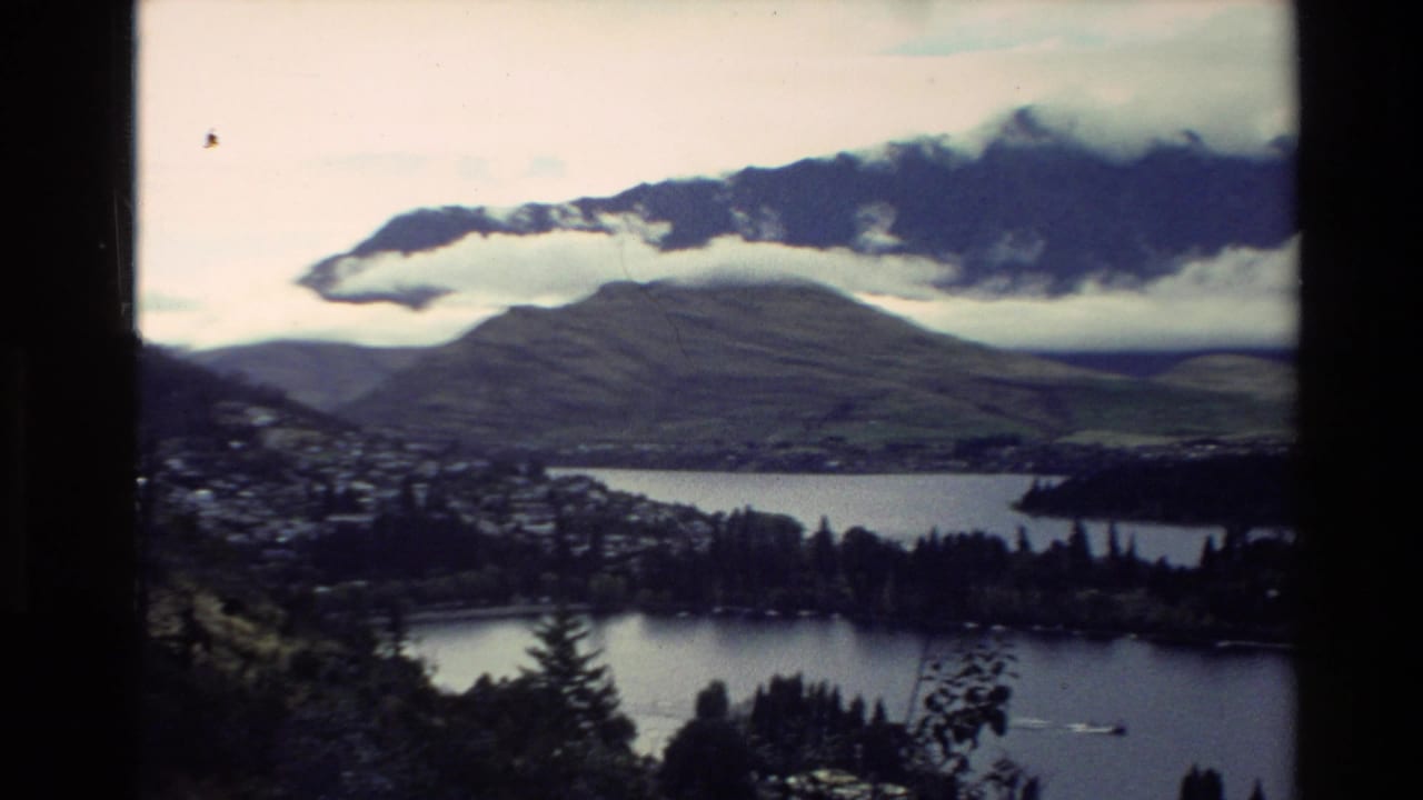 Wide lake overlook with mountains, shoreline town, trees, and low clouds.