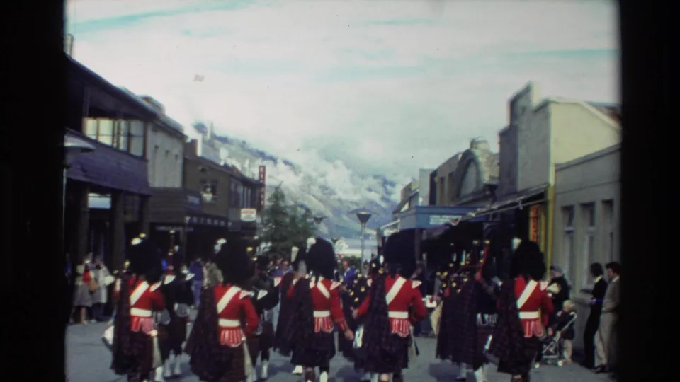 End frame of the New Zealand home movie shows Scottish pipe band members marching away through town while onlookers watch from the sidewalks.