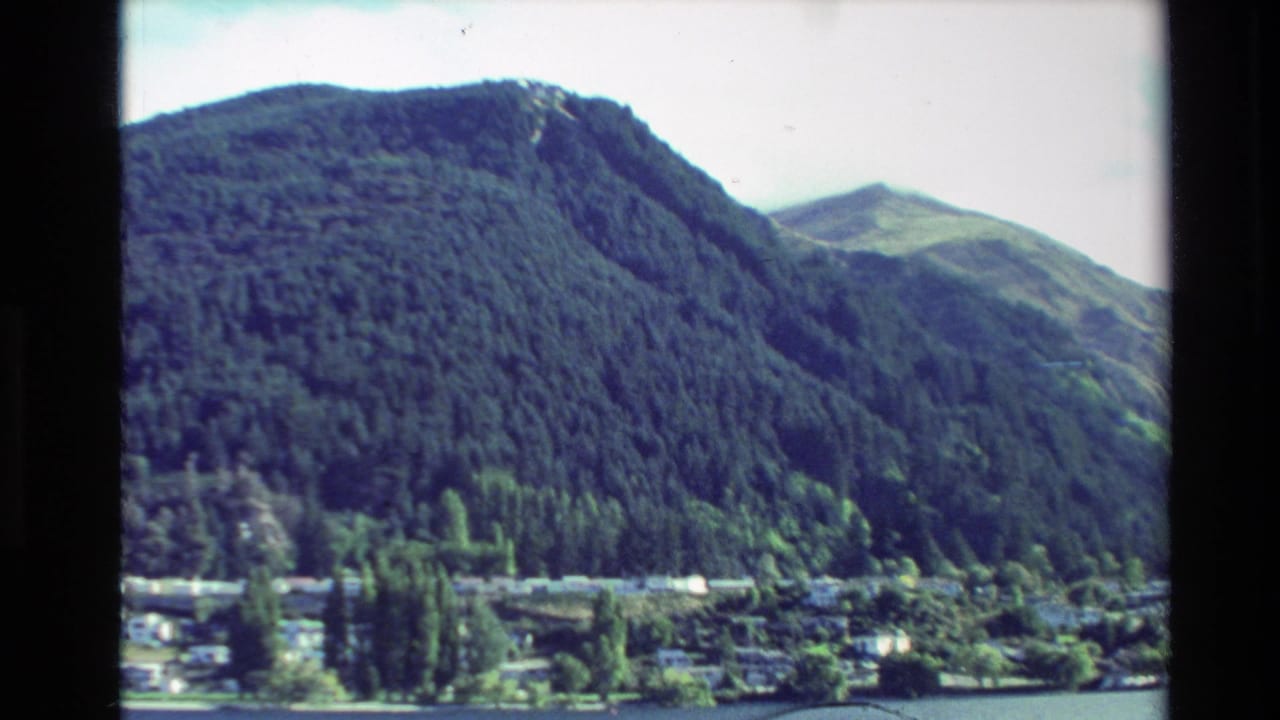 Forested hills rise behind a distant lakeside town across blue water.